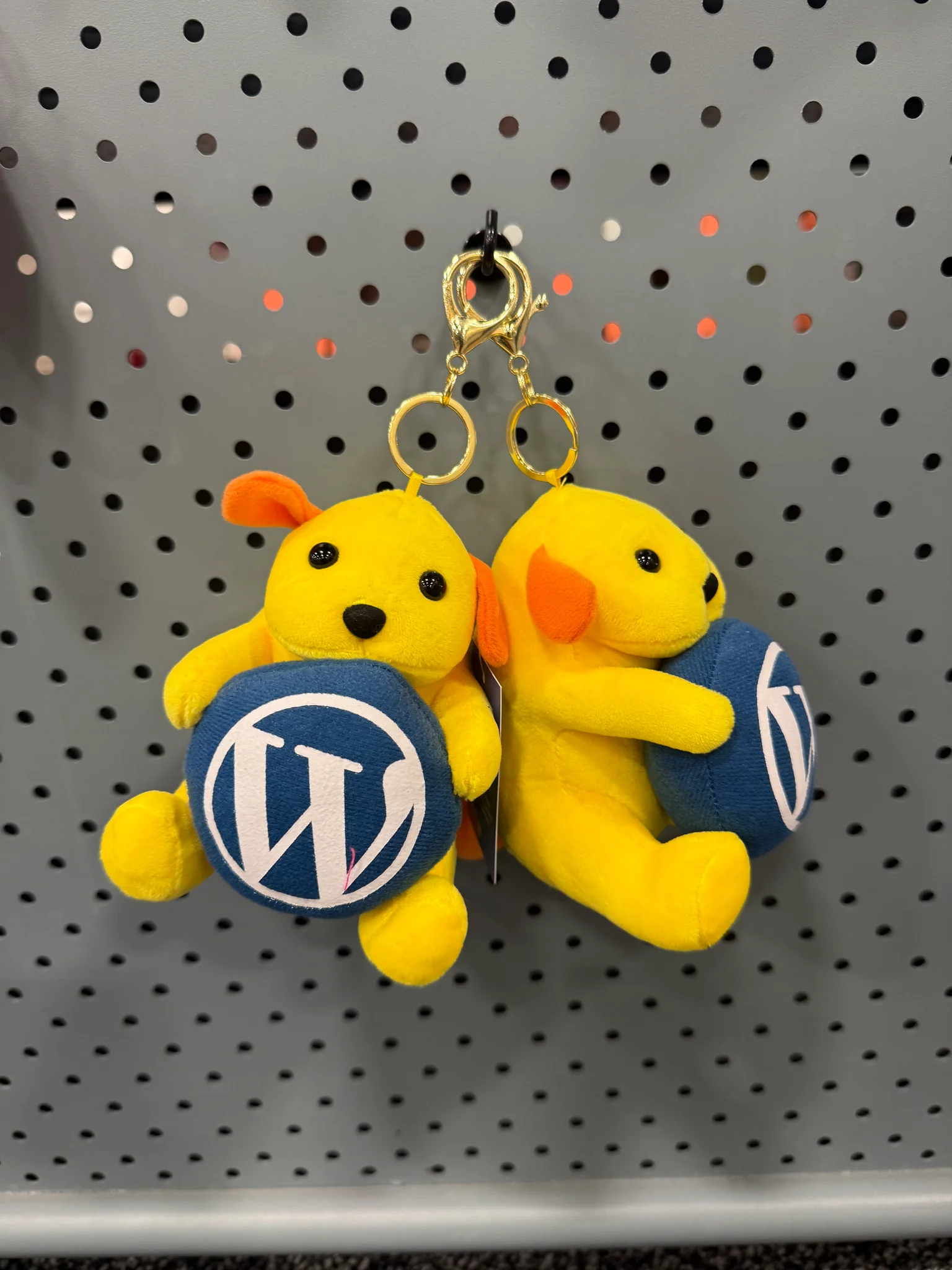 Yellow WordPress plush puppy keychains with W logo hanging on the swag display board